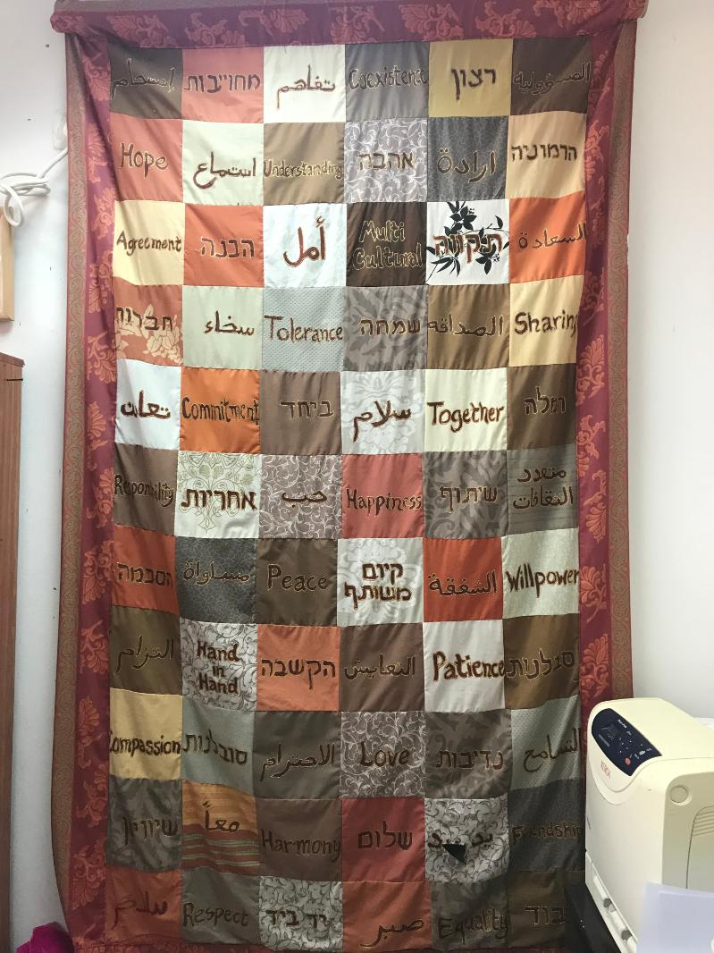 A tapestry on display in a Bilingual kindergarten showing words in Hebrew, Arabic and English.