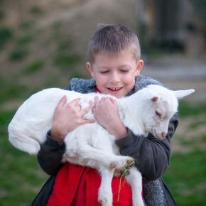 An Eastern Europe child holds a sheep in his arms while smiling