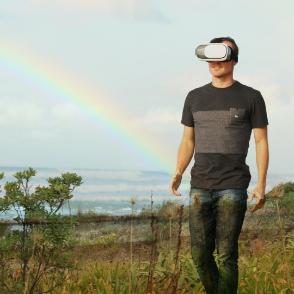 A young male adult walks in a beach wearing a VR headset