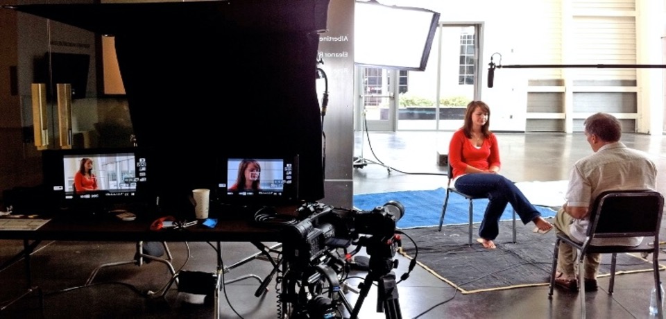 A woman is about to be interviewed by a man in a studio set with two cameras