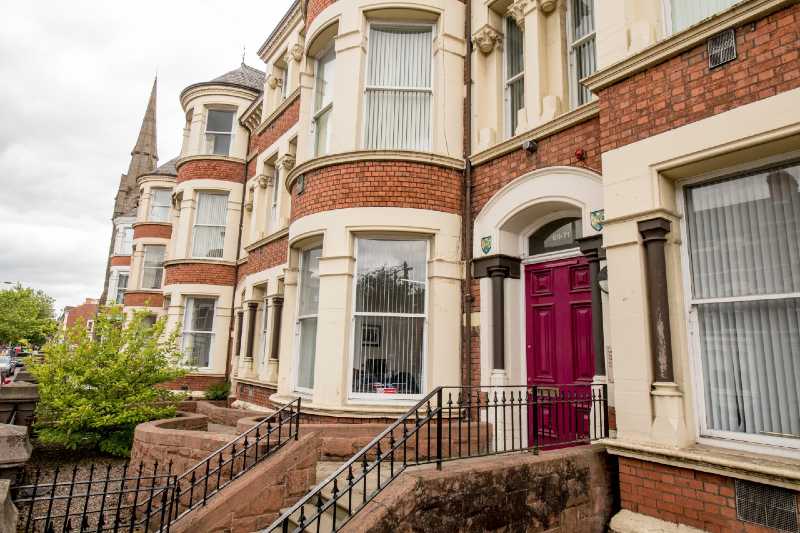 front, side view of three storey building with stone steps up to the front door and railings around the steps and walls