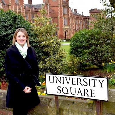 Edel Lamb standing in front of the University Square street sign with the Lanyon building in the distance