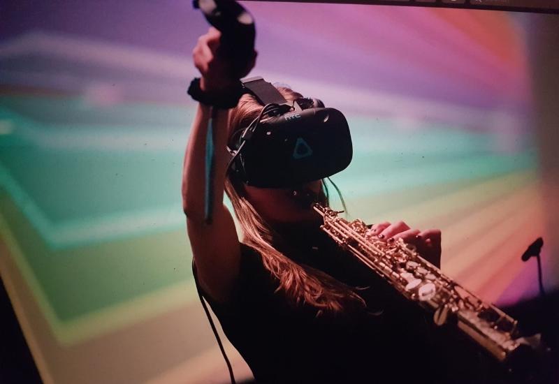 Franziska Schroeder playing soprano saxophone whilst wearing and operating virtual reality equipment