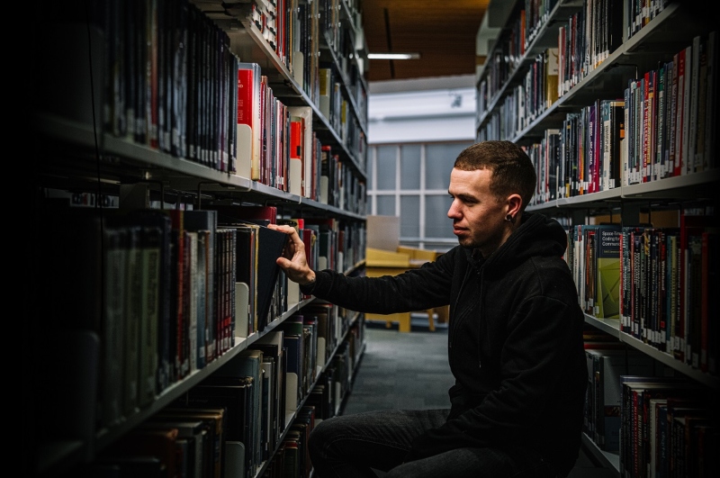 Man on hunkers looking at book stacks in library