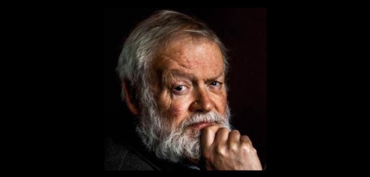 Head and shoulders of Michael Longley, chin resting on his hand and looking directly at the camera over his right shoulder