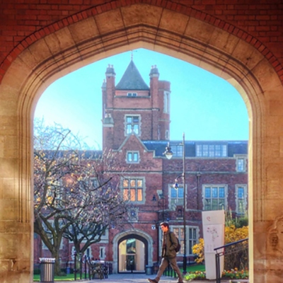 View of the Lanyon tower through a red brick and stone arch. Man with wearing coat and rucksack striding across in foreground