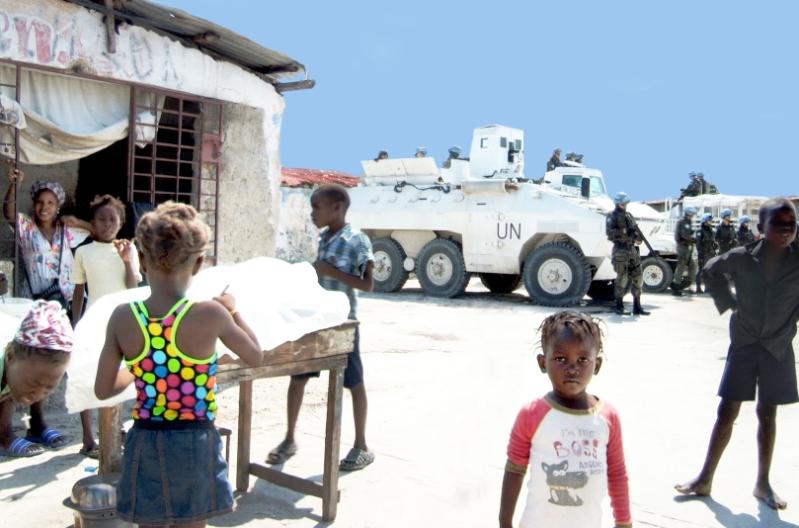 Adults and children in Port-au-Prince working in the sunshine. A small child wearing a red and white t-shirt looks directly at the camera while armed UN troops are gathered beside a tank in the background