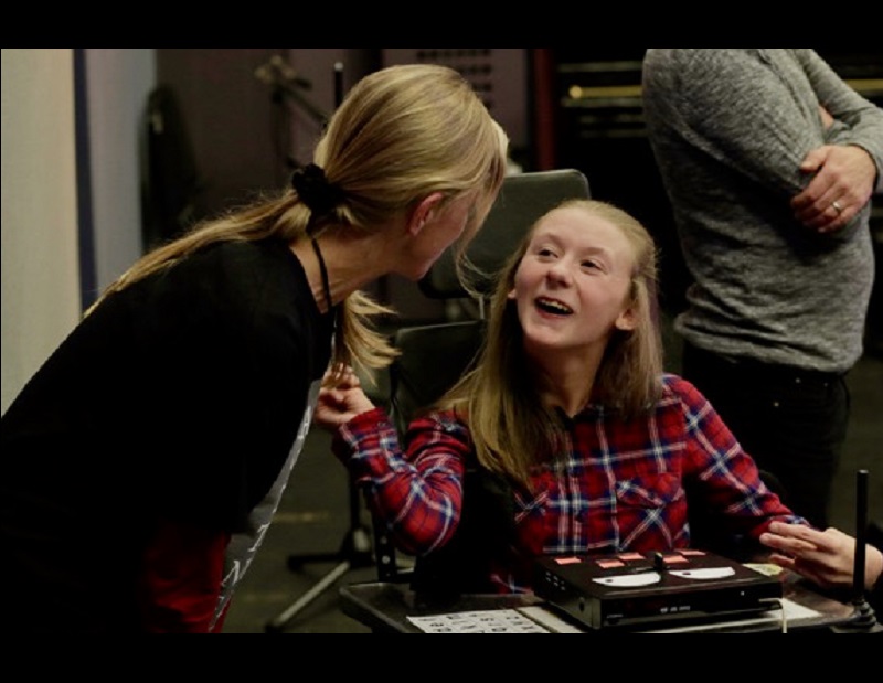 Franziska Schroeder leaning in to young, smiling student who is wearing a red plaid shirt