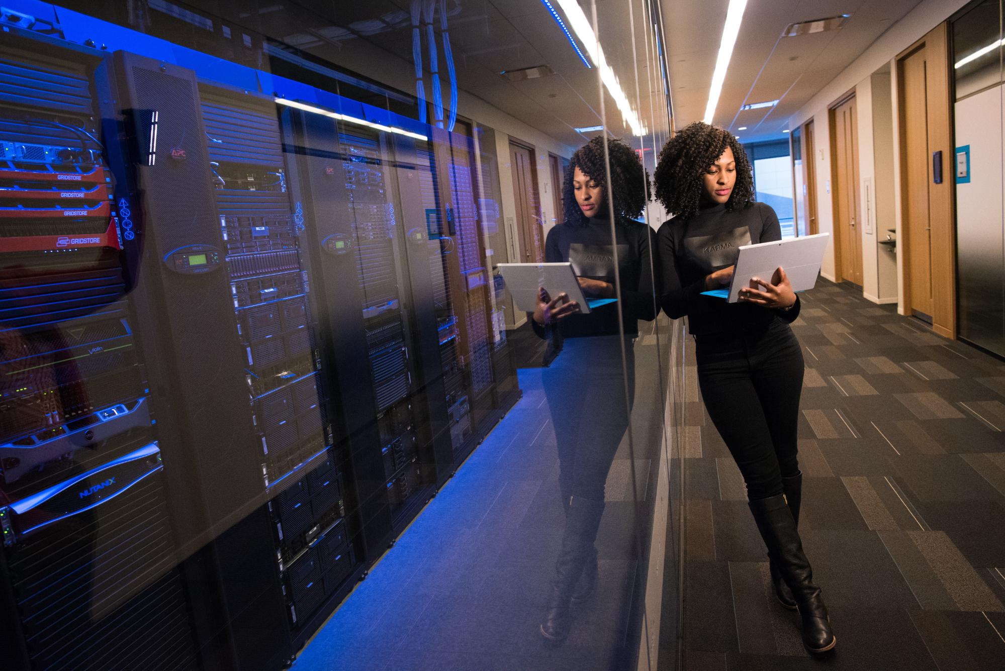 A woman stands with a laptop in front of some servers