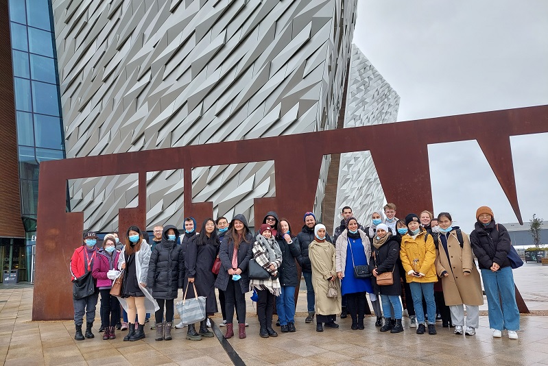 A group of smiling postgraduate students standing in front of a the Titanic Building in Belfast