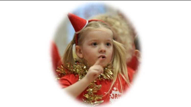 child in a choir wearing a Christmas hat with tinsel around their neck