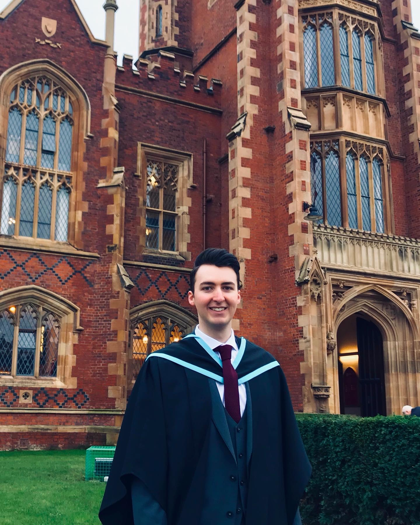 A male student outside Queen's University Belfast on graduation day wearing a graduation gown