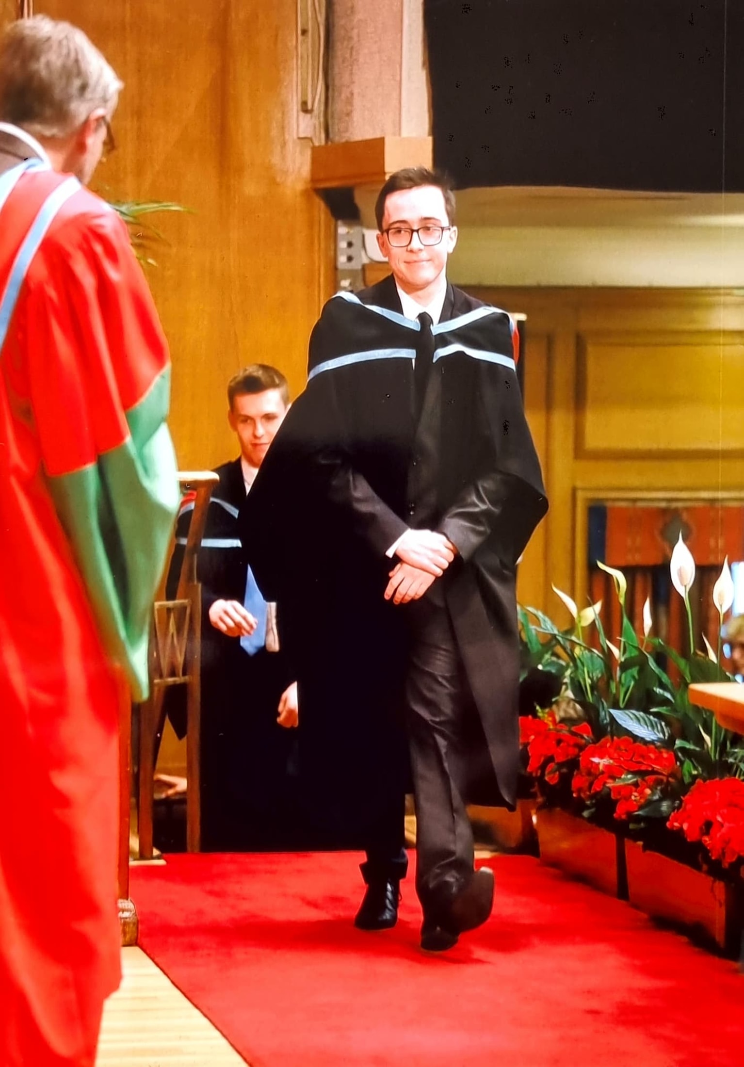 A male student on his graduation day collecing his script, wearing a gown