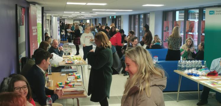 information stands with staff chatting to social work students in a long, glass fronted corridor