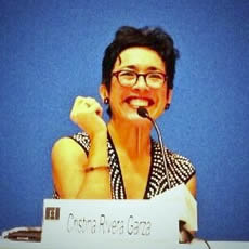 Cristina Rivera Garza smiling at a microphone and holding papers