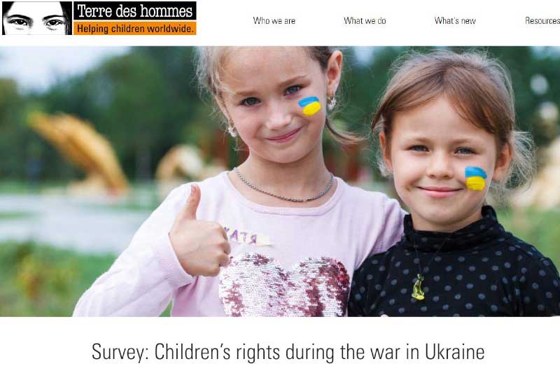 two smiling blond young girls standing close together, with Ukrainian flag colours painted on their cheeks