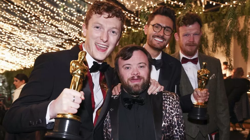 Four males, all wearing evening suits, celebrating winning an Oscar
