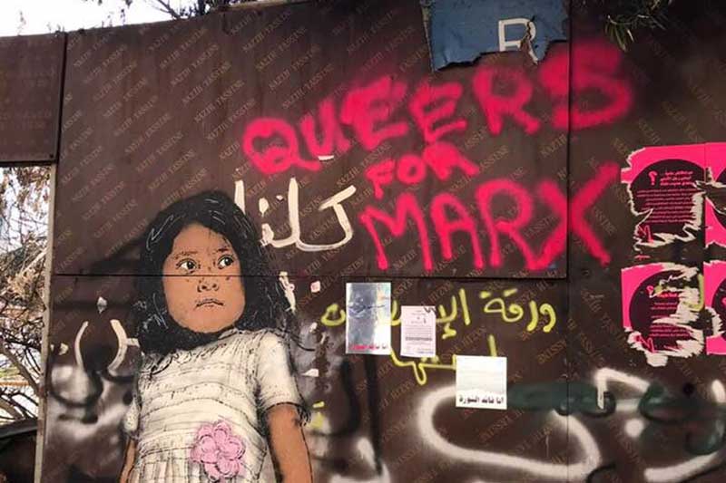 brick wall with painting of a young girl and graffiti 'Queers for Marx'