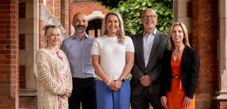 three women and two men in a row under the red brick cloister at Queen's University Belfast