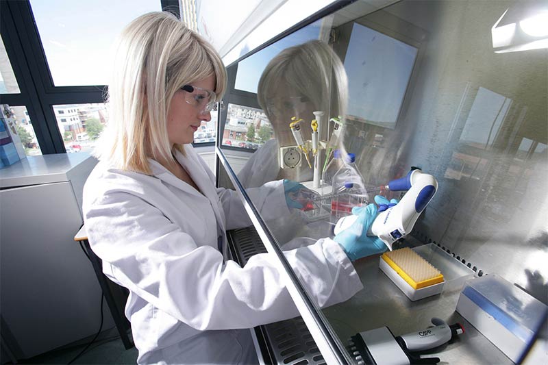 female researcher working in a laboratory from behind a protective screen
