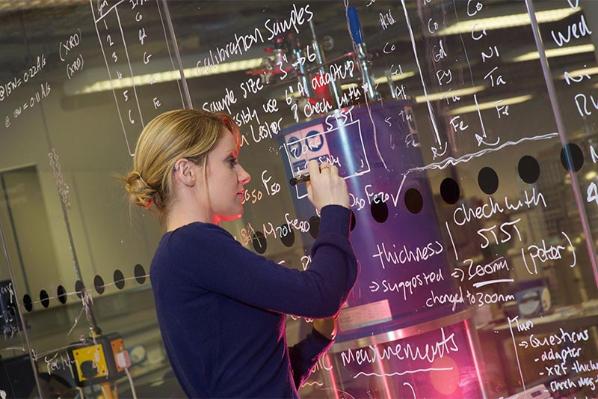 female student writing calculations on a perspex board with white marker