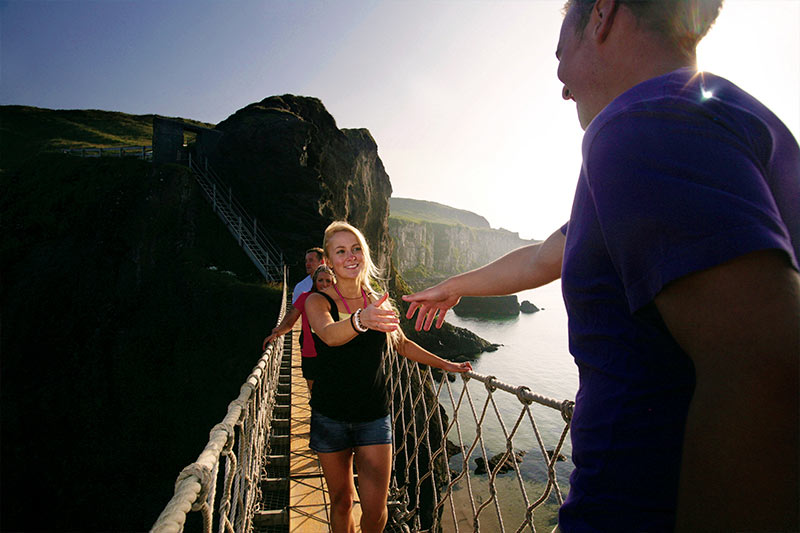 Students crossing carrick-a-rede rope bridge in the sunshine