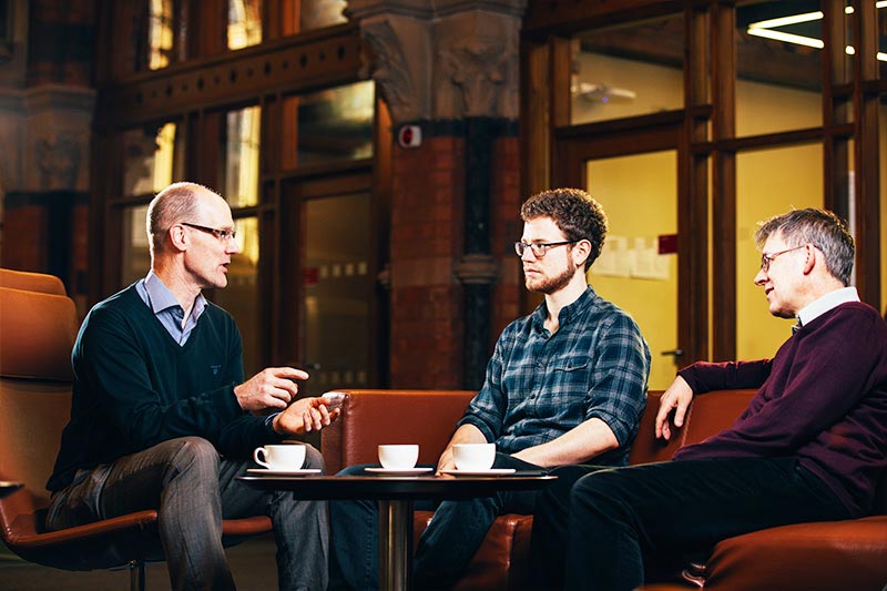 a postgraduate student having a discussion with two academics in the breakout area of the graduate school