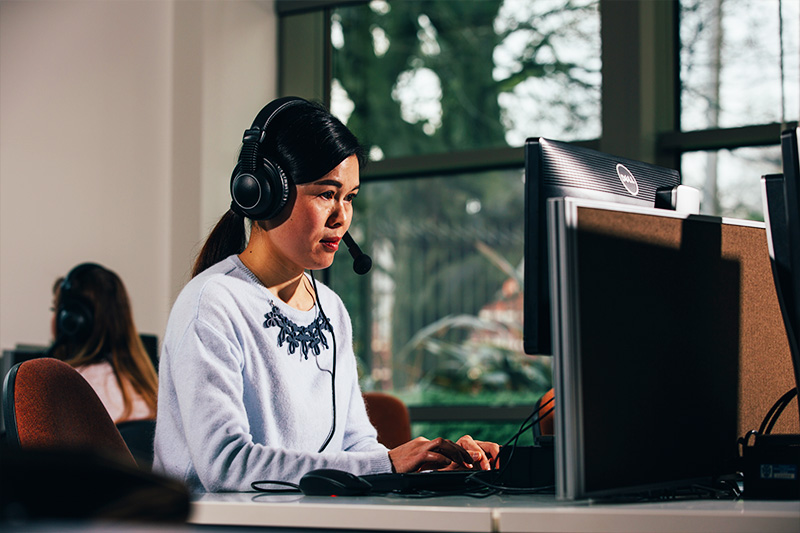 Female student wearing headphones and using a computer in the Queen's Language Centre