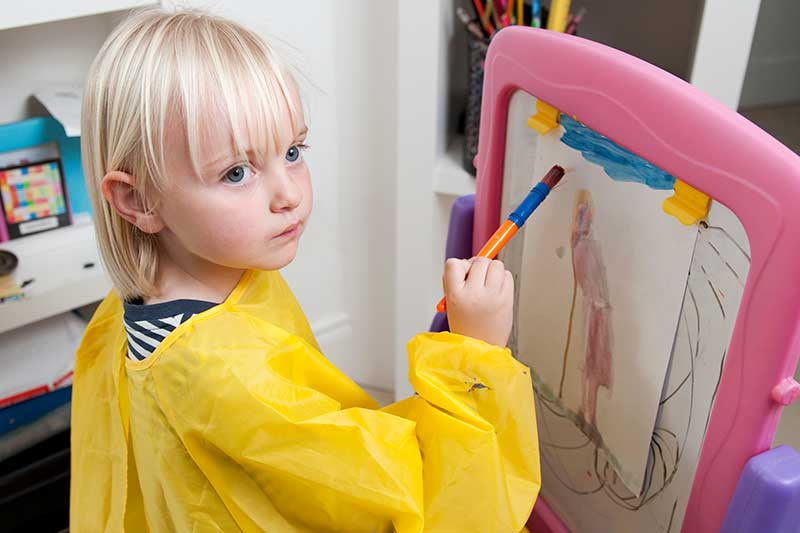 Pre-school aged girl painting at an easel in a school setting.