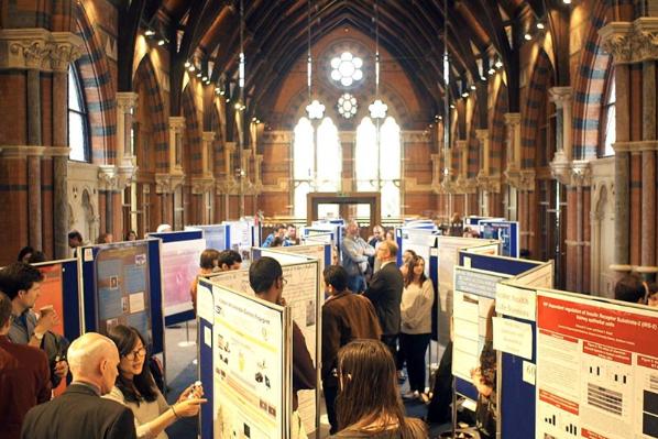 the upper floor of the graduate school filled with posters on boards and students attending a poster competition
