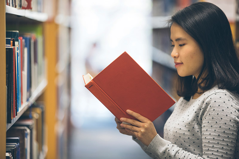 Girl reading a book at library stacks