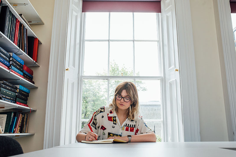 Female student studying in front of large window HAPP