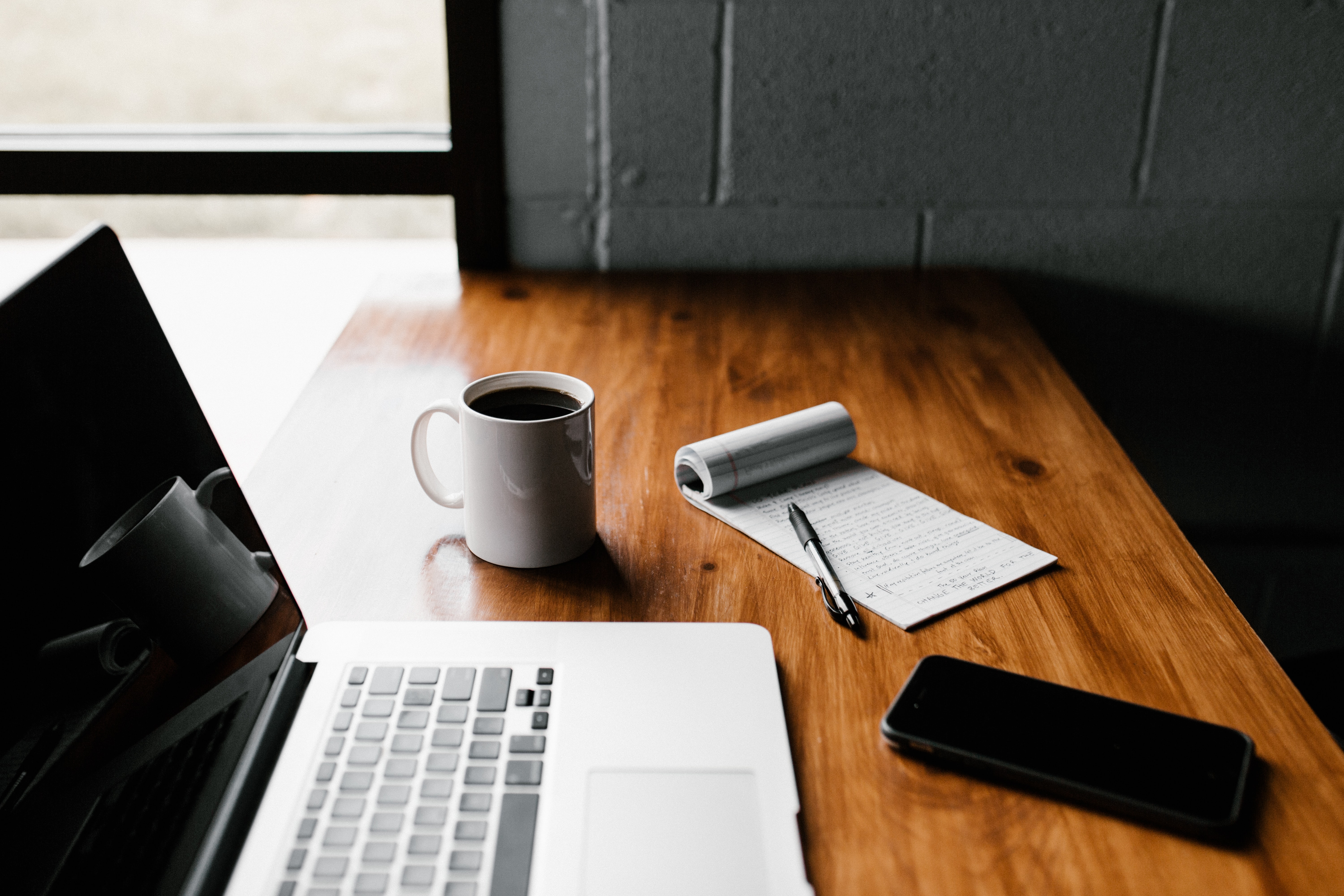 A computer, notebook, and cup of coffee on a table