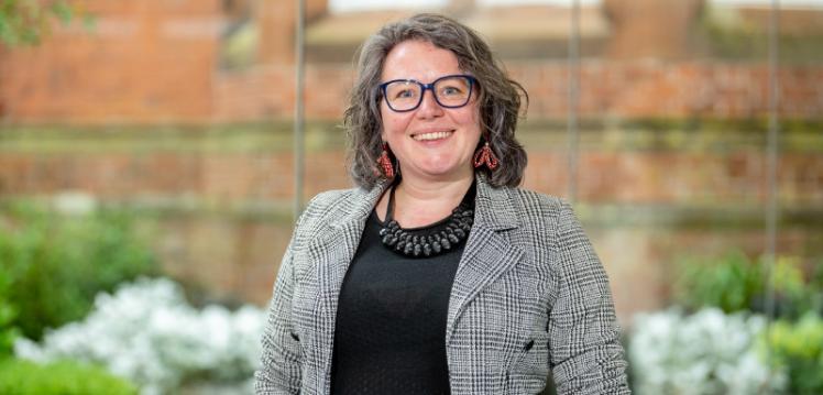 smiling woman with shoulder length wavy hair, a black top and black and white jacket