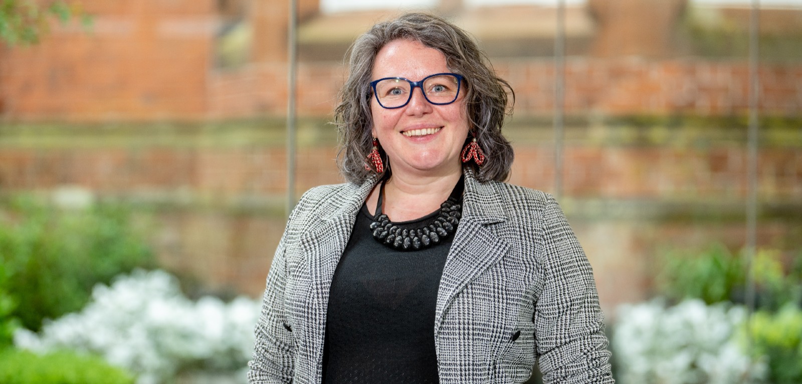 smiling woman with shoulder length wavy hair, a black top and black and white jacket