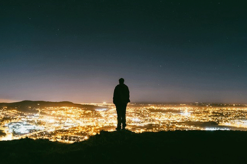 a man standing on a hill at night with city lights below