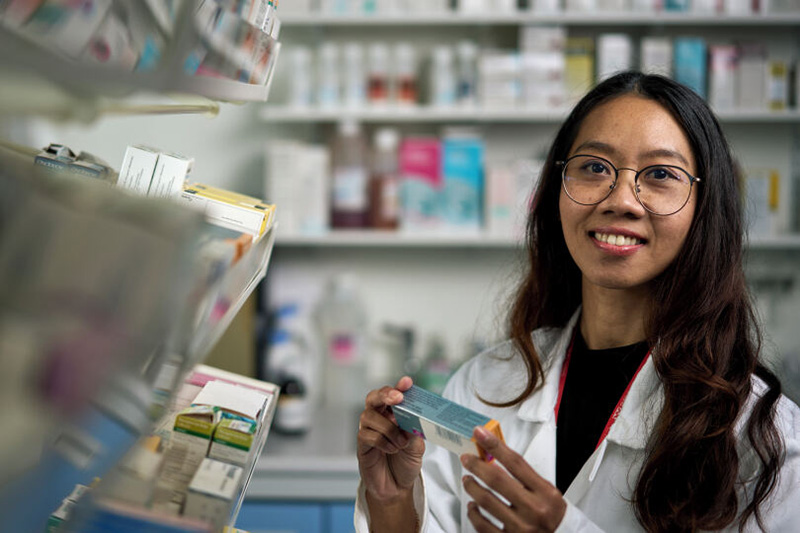 A pharmacist standing beside a shelf of medicines