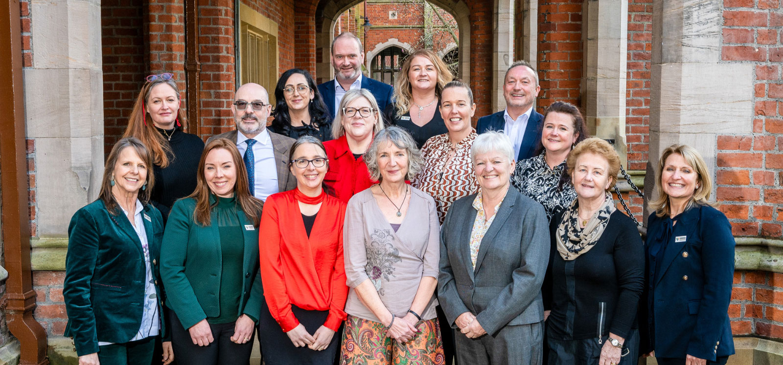 two rows of men and women with a red brick wall and arch background