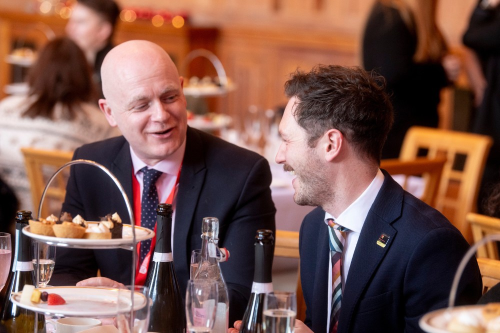 two seated men chatting at a table at an indoor afternoon tea event