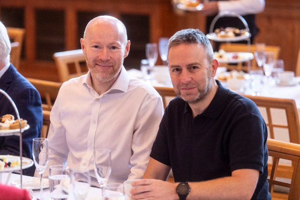 two seated men smiling to camera at an indoor event