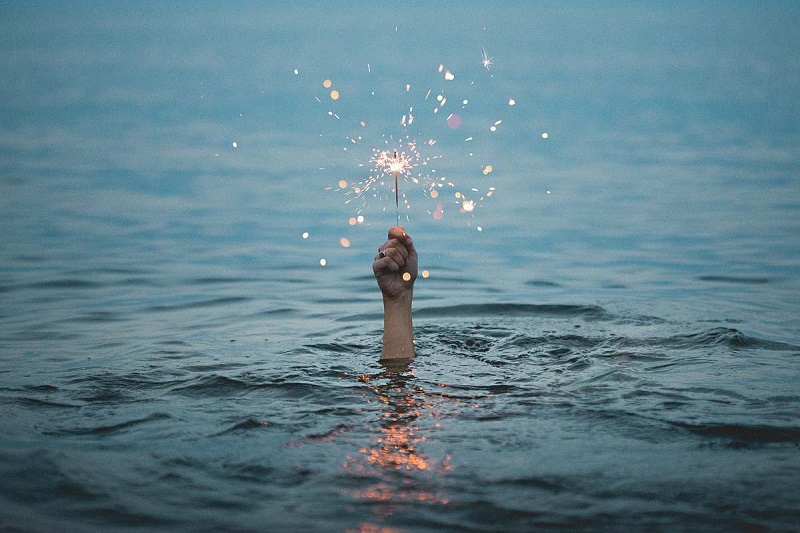Person submerged under body of water holding sparkler