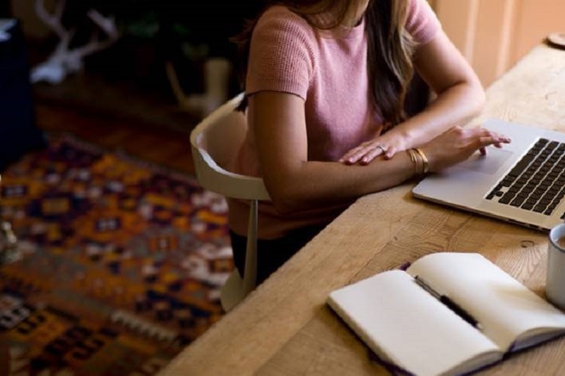 Woman working at home on laptop and with notebook and pen