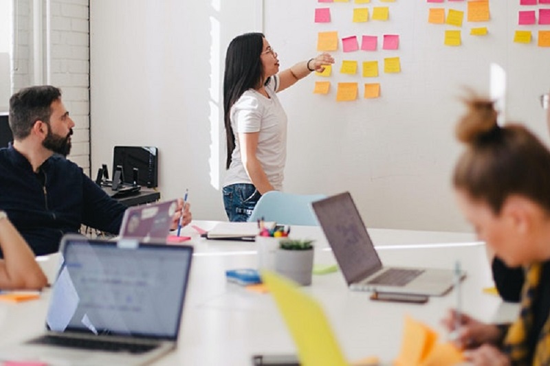 young woman pointing to sticky notes on a wall with a man and woman listening