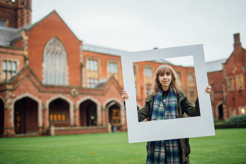 Image of student in the quadrangle holding up large polaroid frame