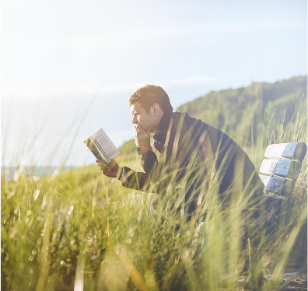 Man sitting in a field while reading a book