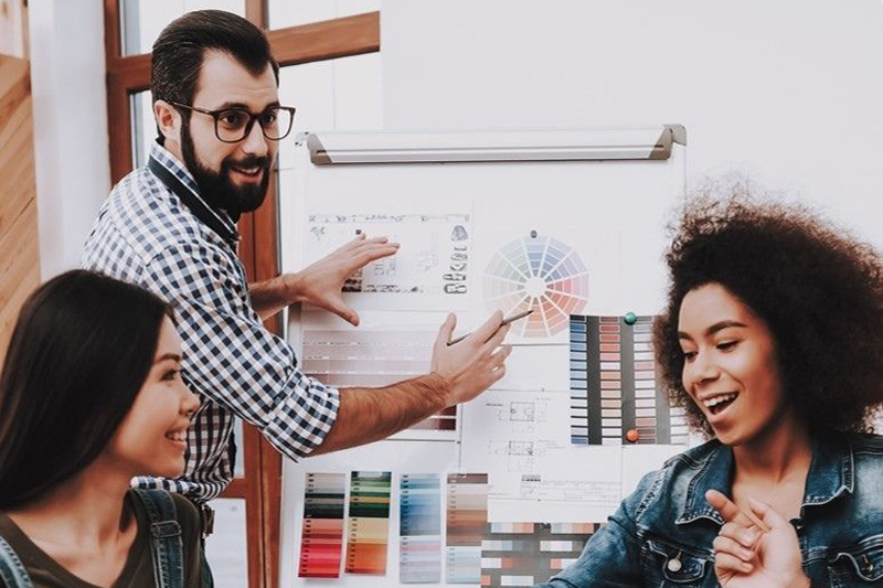 Man at whiteboard and two female workers enjoying a design thinking workshop