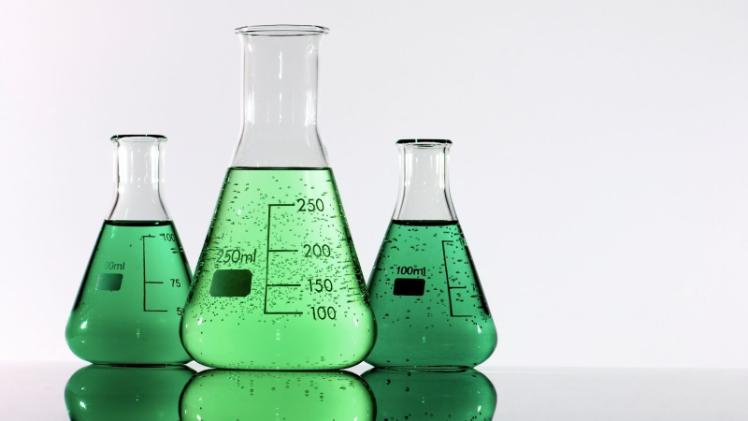 three conical flasks - one large, two small - containing opaque green liquid