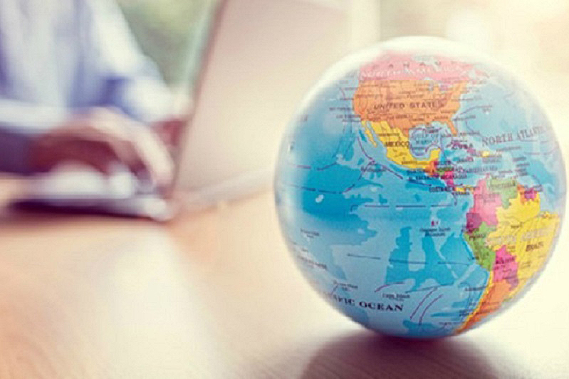 globe on desk with person in background working on laptop
