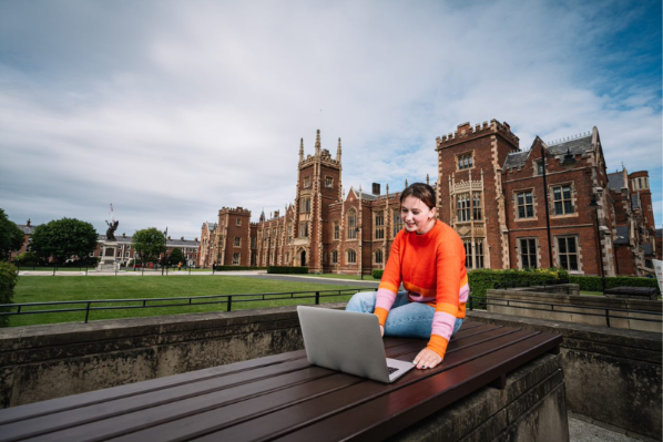 feale student sitting outside Queen's University on a laptop