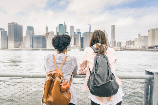 two females standing on a boat looking out and seeing New York skyline